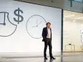 Un homme en costume présente une conférence pecha kucha. Des horloges et un symbole dollar sur l'écran suggèrent le thème du temps et de l'argent.
