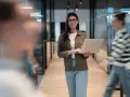Une program manager concentrée, portable à la main, traverse un couloir d'entreprise moderne.