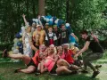 Un groupe de personnes célèbre une **activité team building plein air** avec des ballons et des trophées. Ils sont joyeux et pleins d'énergie.