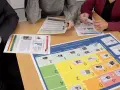 Des personnes analysent des documents et un plateau de jeu de rôle management. Ils discutent des performances et de l'importance des enjeux.