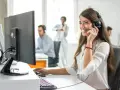 Une opératrice souriante gère l'accueil téléphonique d'une entreprise, casque sur les oreilles, devant son écran.