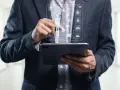 Un homme en costume utilise une tablette pour visualiser un tableau de bord de santé, marquant la cloture de projet.