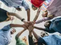 Une équipe diverse célèbre une réussite lors d'une activité de groupe, mains jointes au centre.