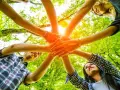 Des mains s'unissent dans un cercle, symbolisant un jeu ludique adulte en pleine nature.