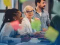 Une équipe discute autour d'une table, la chef de projet souriante au centre. Des post-its colorés flottent, symbolisant la créativité et la collaboration.