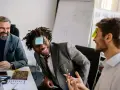 Un homme rit avec une note "Dog" sur le front, participant à un jeu de communication d'équipe.