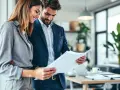 Un couple d'affaires examine des documents, illustrant une gestion multi projet réussie dans un bureau moderne.