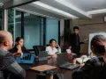 Une équipe discute de stratégies de management et communication autour d'une table de réunion. Un homme présente des graphiques sur un écran.
