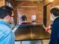 Des hommes jouent au ping-pong, une activité de jeux d'intérieur en groupe, dans un bureau moderne avec des murs en briques.