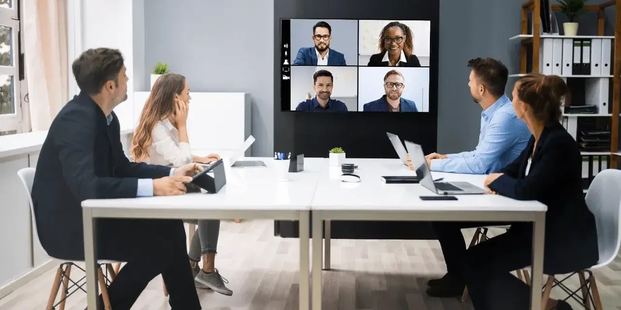 Une équipe en visioconférence, illustrant le futur du travail. Des collègues échangent à distance, connectés via un écran mural.