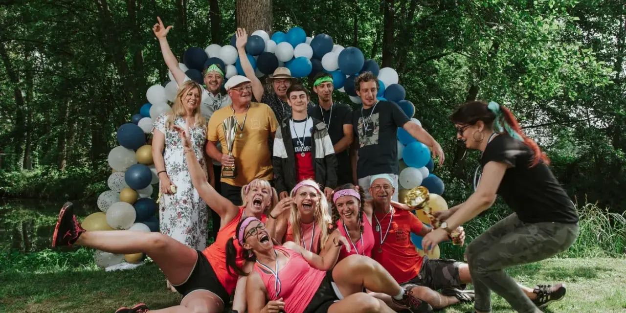 Un groupe de personnes célèbre une **activité team building plein air** avec des ballons et des trophées. Ils sont joyeux et pleins d'énergie.