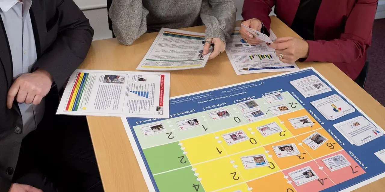 Des personnes analysent des documents et un plateau de jeu de rôle management. Ils discutent des performances et de l'importance des enjeux.