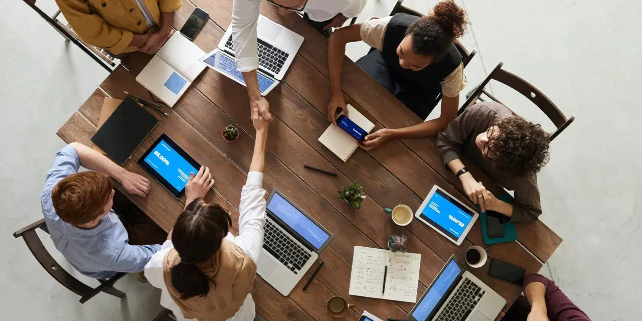 Une équipe diversifiée collabore autour d'une table en bois, renforçant la communication et la cohésion d'équipe par des poignées de main et des discussions.