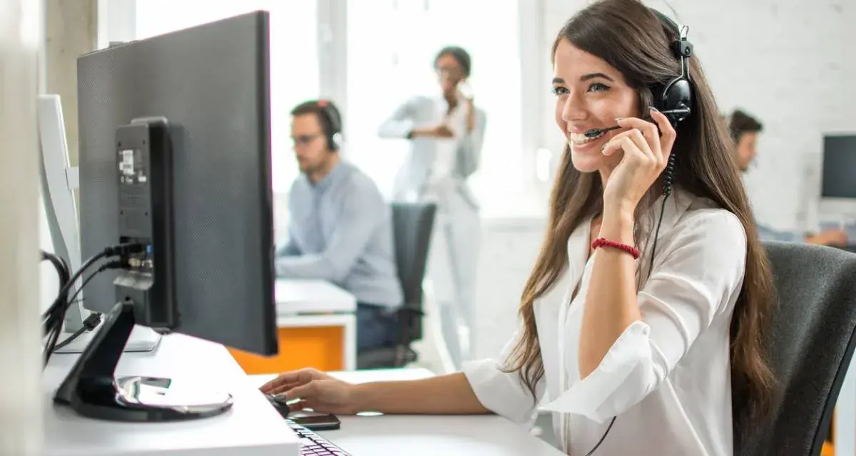 Une opératrice souriante gère l'accueil téléphonique d'une entreprise, casque sur les oreilles, devant son écran.