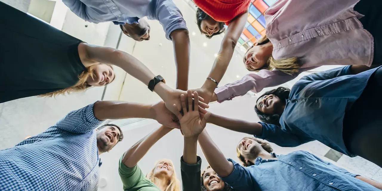 Une équipe diverse célèbre une réussite lors d'une activité de groupe, mains jointes au centre.