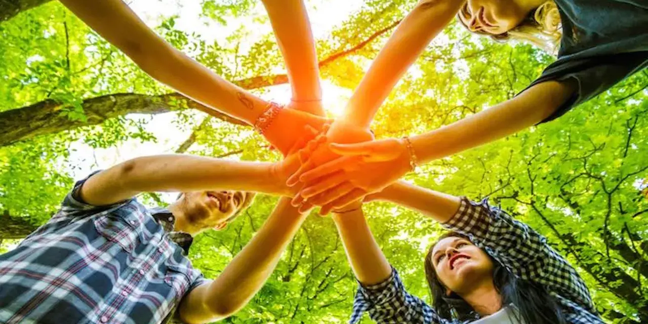 Des mains s'unissent dans un cercle, symbolisant un jeu ludique adulte en pleine nature.