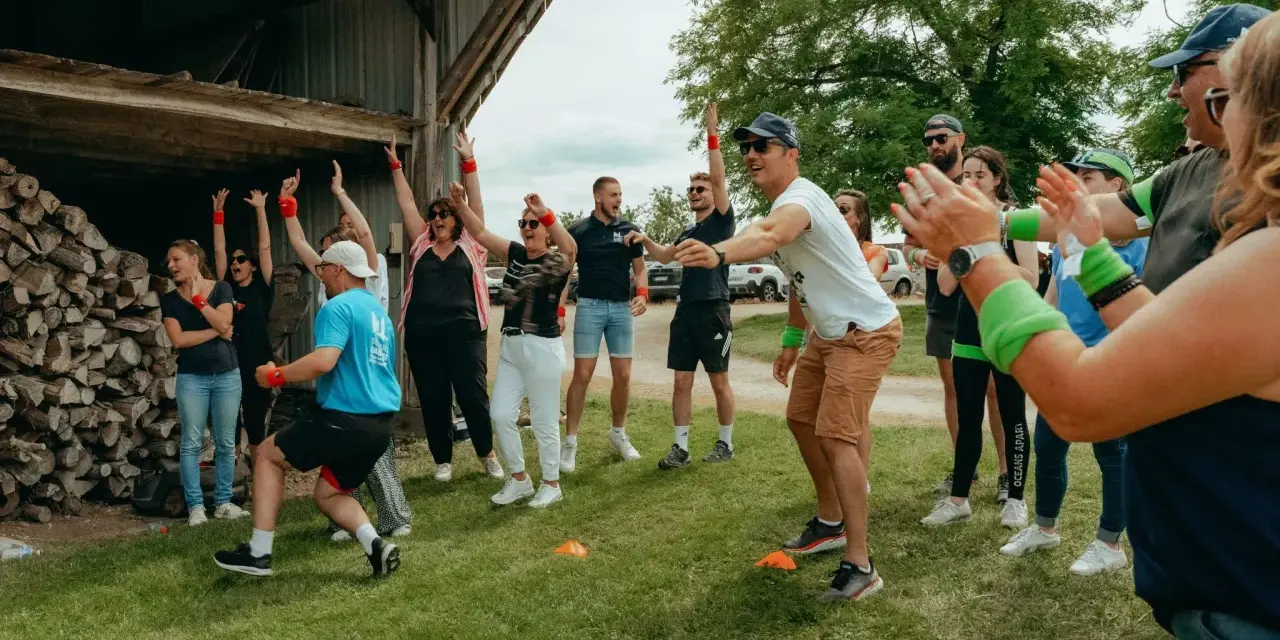 Des participants enthousiastes s'amusent lors d'un événement de team building jeux olympiques, bras levés et souriants.