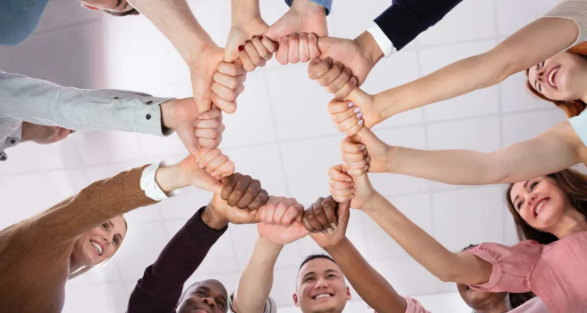 Un cercle de mains jointes symbolise la dynamique d'équipe et la solidarité. Des sourires illuminent les visages, reflétant la joie du travail collaboratif.