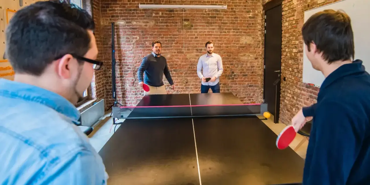 Des hommes jouent au ping-pong, une activité de jeux d'intérieur en groupe, dans un bureau moderne avec des murs en briques.