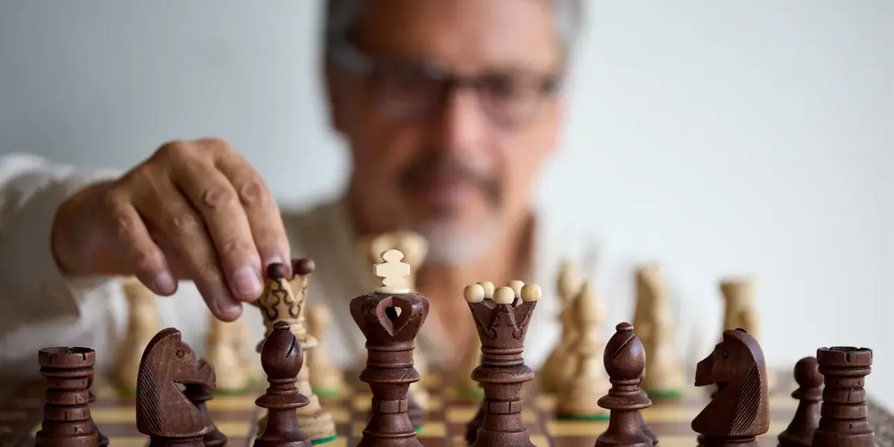 Un homme réfléchit, une pièce d'échecs à la main. Il faut avoir un esprit critique pour anticiper chaque mouvement.