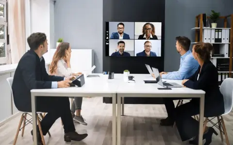 Une équipe en visioconférence, illustrant le futur du travail. Des collègues échangent à distance, connectés via un écran mural.