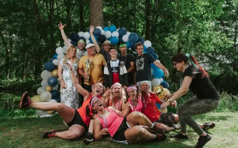 Un groupe de personnes célèbre une **activité team building plein air** avec des ballons et des trophées. Ils sont joyeux et pleins d'énergie.