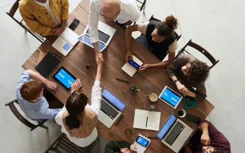 Une équipe diversifiée collabore autour d'une table en bois, renforçant la communication et la cohésion d'équipe par des poignées de main et des discussions.
