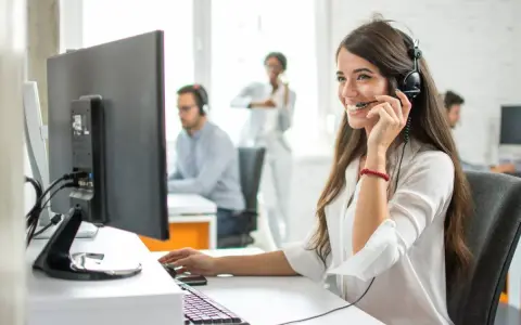 Une opératrice souriante gère l'accueil téléphonique d'une entreprise, casque sur les oreilles, devant son écran.