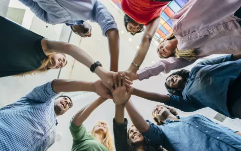Une équipe diverse célèbre une réussite lors d'une activité de groupe, mains jointes au centre.