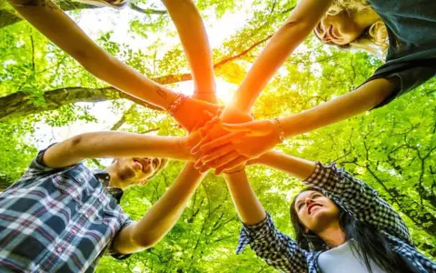 Des mains s'unissent dans un cercle, symbolisant un jeu ludique adulte en pleine nature.