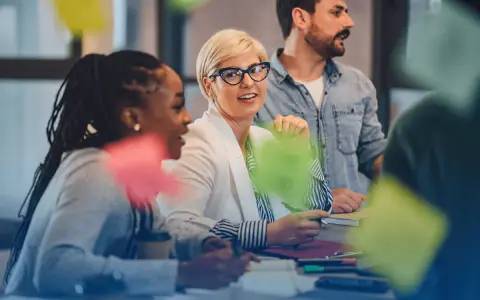 Une équipe discute autour d'une table, la chef de projet souriante au centre. Des post-its colorés flottent, symbolisant la créativité et la collaboration.