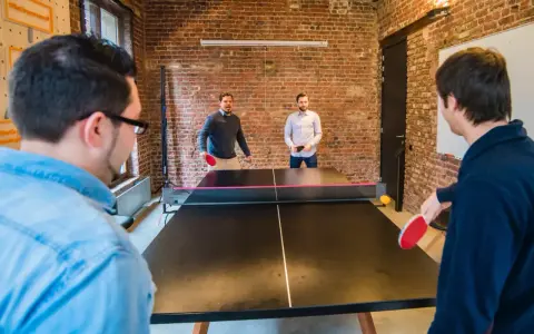 Des hommes jouent au ping-pong, une activité de jeux d'intérieur en groupe, dans un bureau moderne avec des murs en briques.