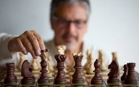 Un homme réfléchit, une pièce d'échecs à la main. Il faut avoir un esprit critique pour anticiper chaque mouvement.