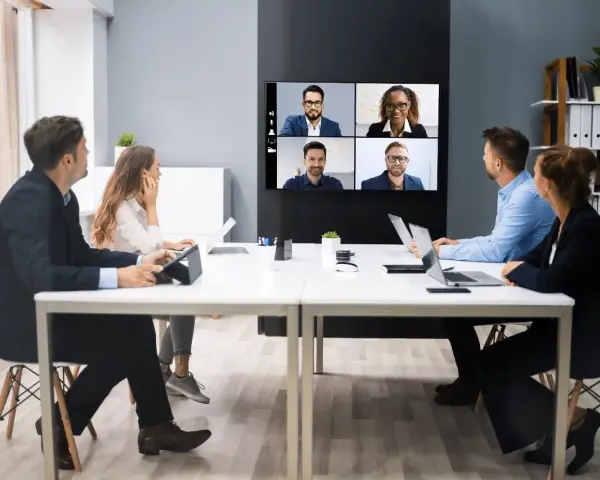 Une équipe en visioconférence, illustrant le futur du travail. Des collègues échangent à distance, connectés via un écran mural.