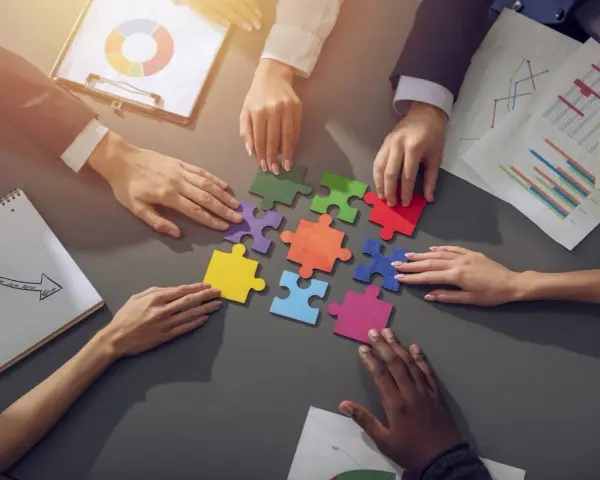 Des mains assemblent des pièces de puzzle colorées, symbolisant la collaboration en équipe. Des graphiques et un bloc-notes complètent la scène.