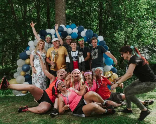 Un groupe de personnes célèbre une **activité team building plein air** avec des ballons et des trophées. Ils sont joyeux et pleins d'énergie.