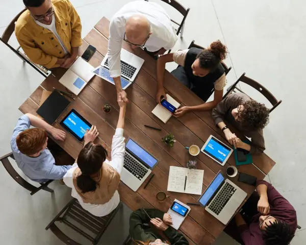 Une équipe diversifiée collabore autour d'une table en bois, renforçant la communication et la cohésion d'équipe par des poignées de main et des discussions.