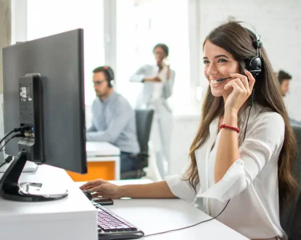 Une opératrice souriante gère l'accueil téléphonique d'une entreprise, casque sur les oreilles, devant son écran.