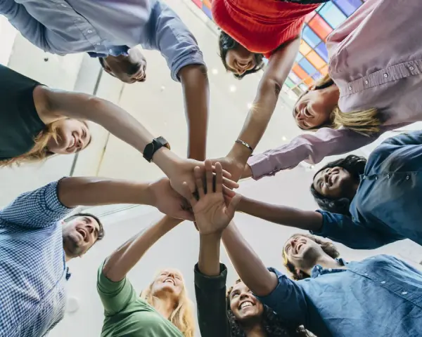 Une équipe diverse célèbre une réussite lors d'une activité de groupe, mains jointes au centre.