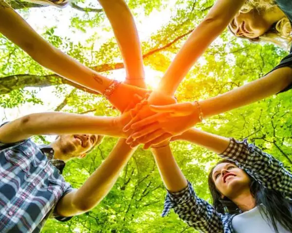 Des mains s'unissent dans un cercle, symbolisant un jeu ludique adulte en pleine nature.
