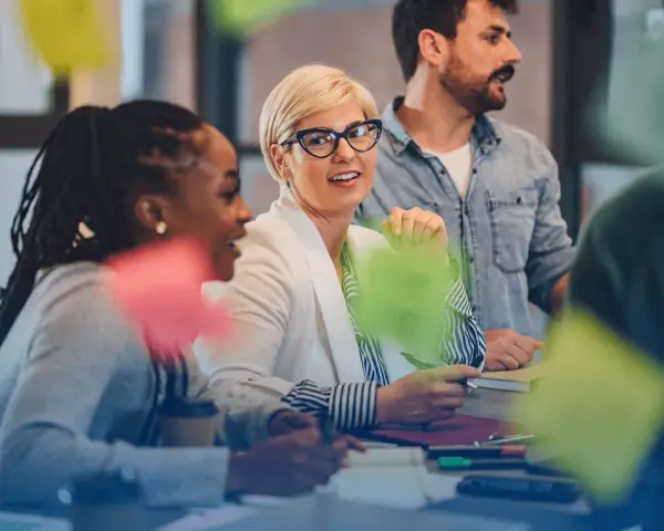 Une équipe discute autour d'une table, la chef de projet souriante au centre. Des post-its colorés flottent, symbolisant la créativité et la collaboration.