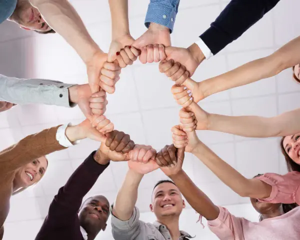 Un cercle de mains jointes symbolise la dynamique d'équipe et la solidarité. Des sourires illuminent les visages, reflétant la joie du travail collaboratif.