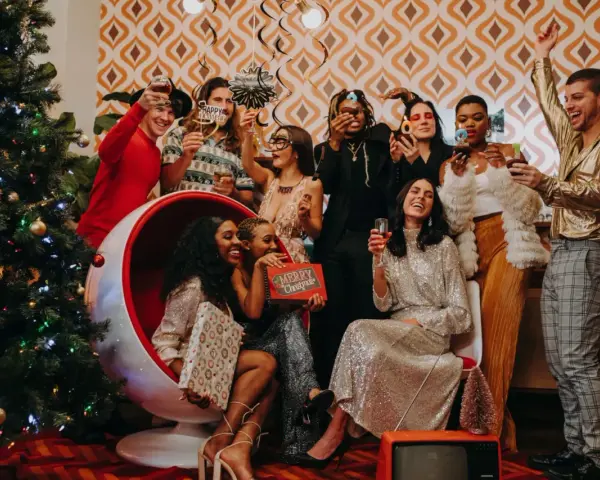 Ambiance festive pour une soirée de Noël entreprise : un groupe d'amis pétillants trinque près d'un sapin décoré, dans une atmosphère rétro et joyeuse.