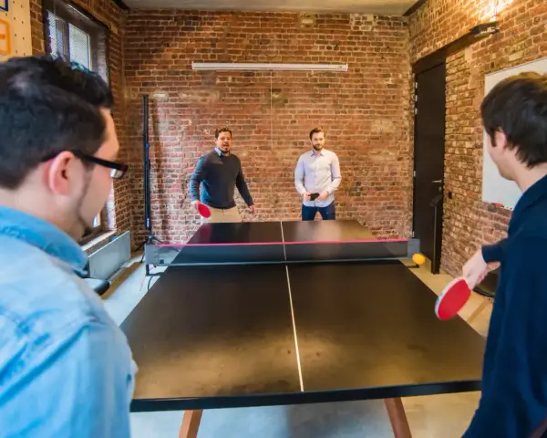 Des hommes jouent au ping-pong, une activité de jeux d'intérieur en groupe, dans un bureau moderne avec des murs en briques.