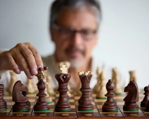 Un homme réfléchit, une pièce d'échecs à la main. Il faut avoir un esprit critique pour anticiper chaque mouvement.