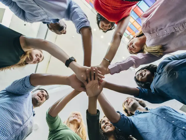 Une équipe diverse célèbre une réussite lors d'une activité de groupe, mains jointes au centre.