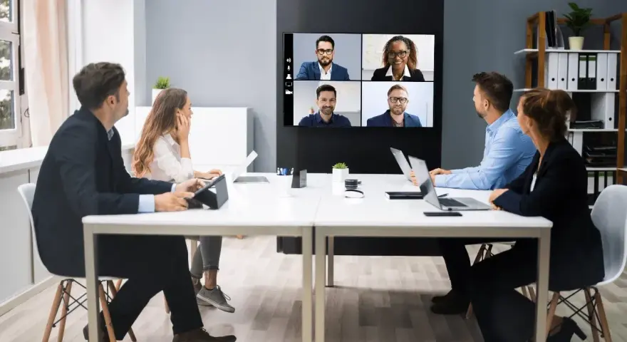 Une équipe en visioconférence, illustrant le futur du travail. Des collègues échangent à distance, connectés via un écran mural.