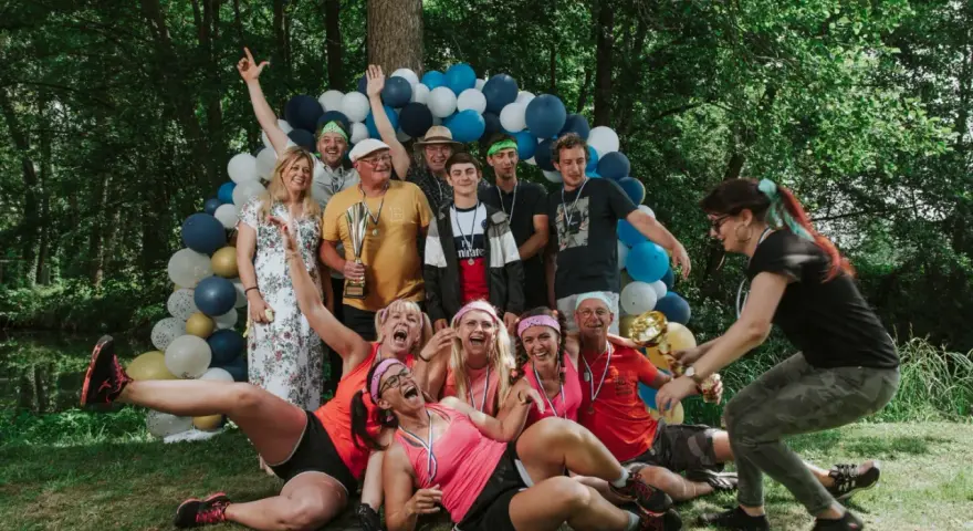 Un groupe de personnes célèbre une **activité team building plein air** avec des ballons et des trophées. Ils sont joyeux et pleins d'énergie.