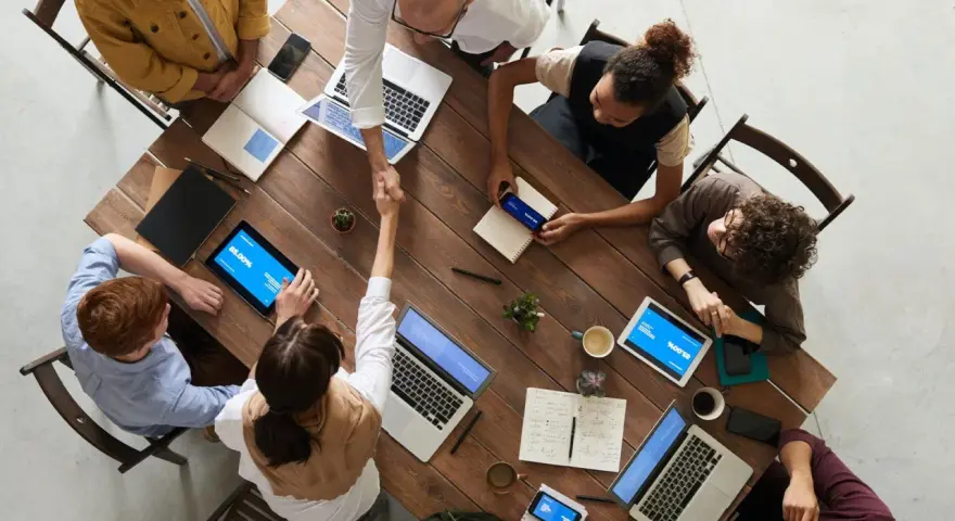 Une équipe diversifiée collabore autour d'une table en bois, renforçant la communication et la cohésion d'équipe par des poignées de main et des discussions.