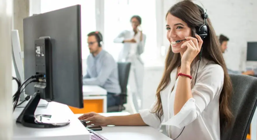 Une opératrice souriante gère l'accueil téléphonique d'une entreprise, casque sur les oreilles, devant son écran.